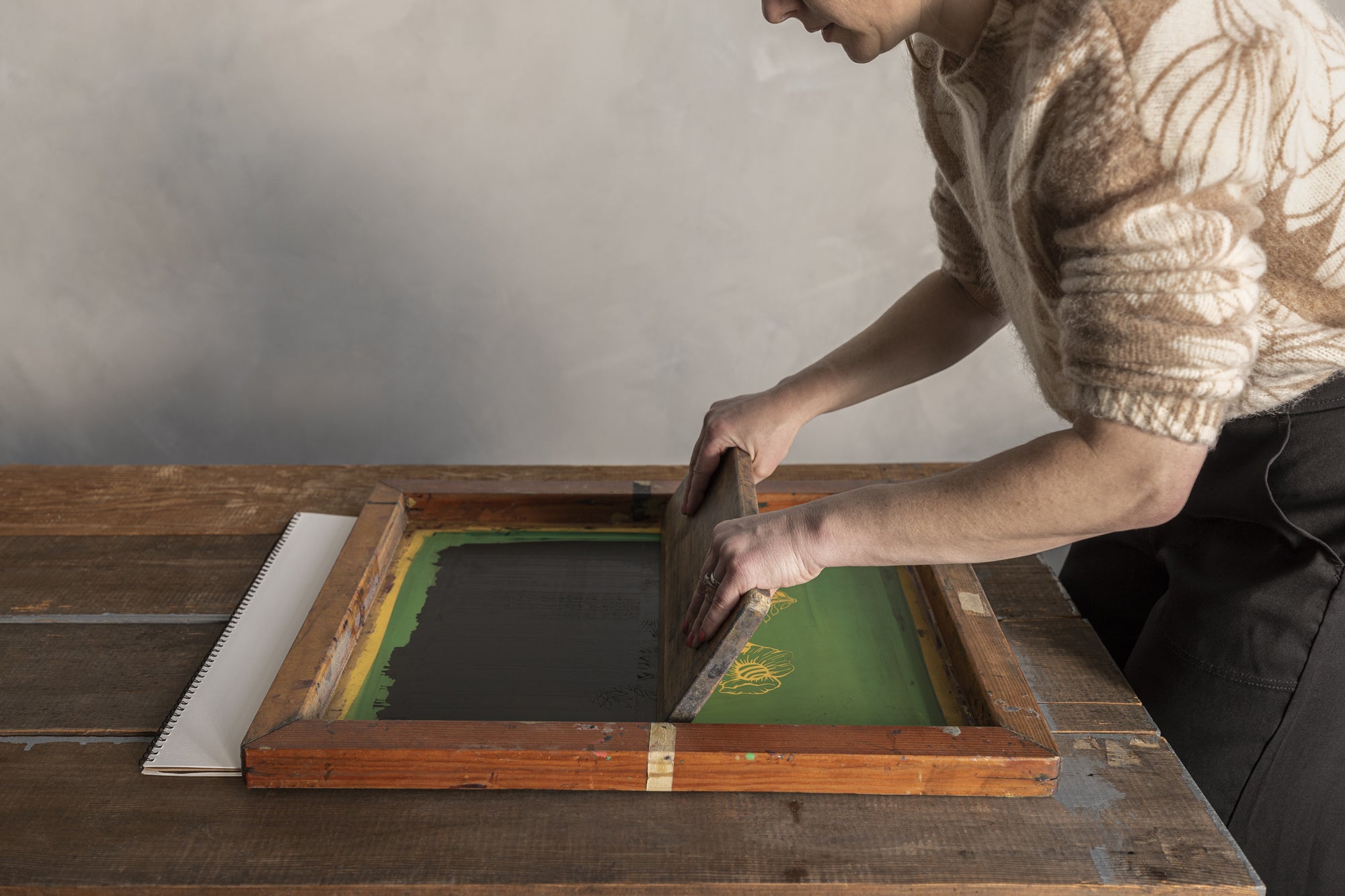 Woman artist screenpainting black paint over green.