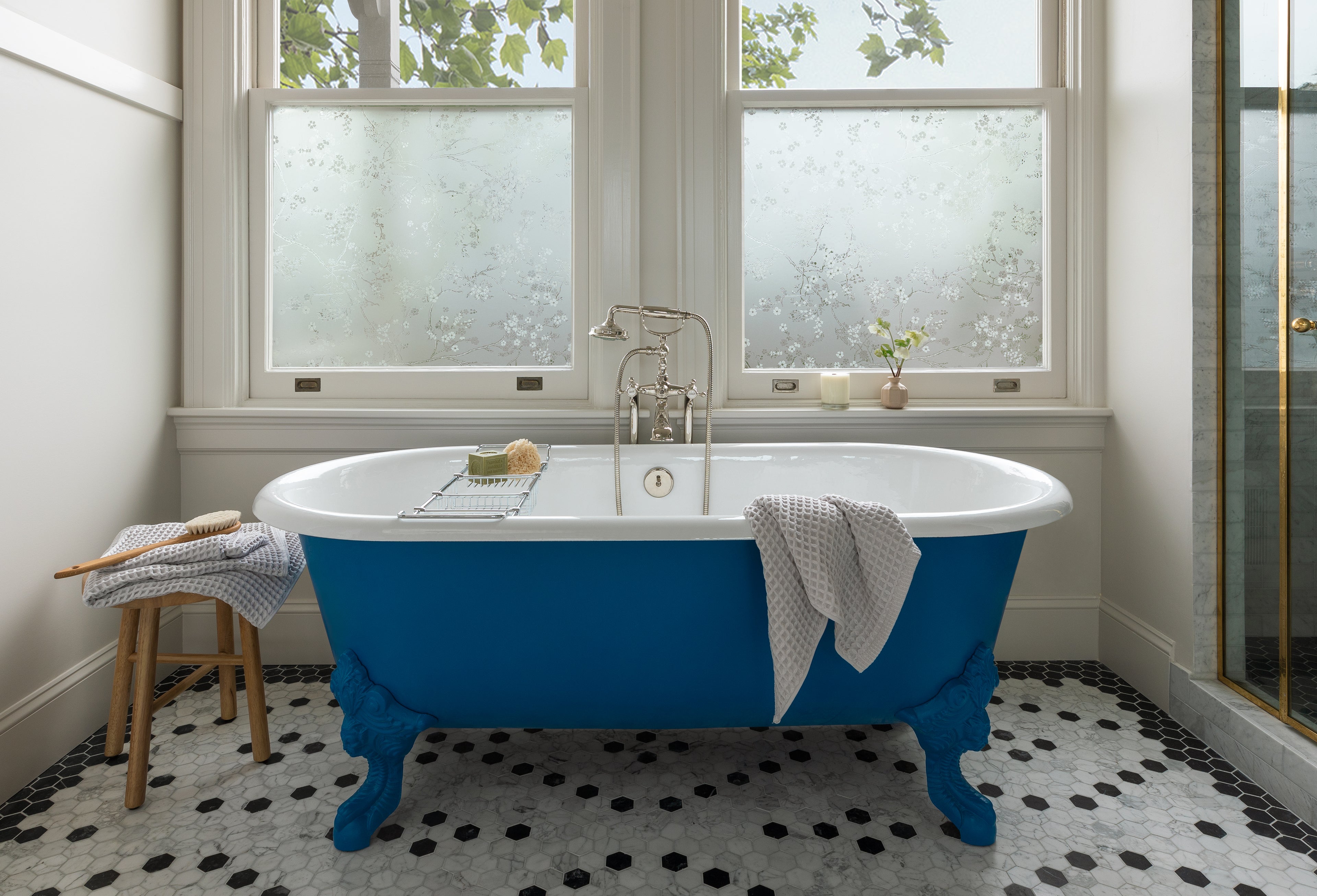 Blue bathtub in front of 2 side by side windows in bathroom in shades of white.
