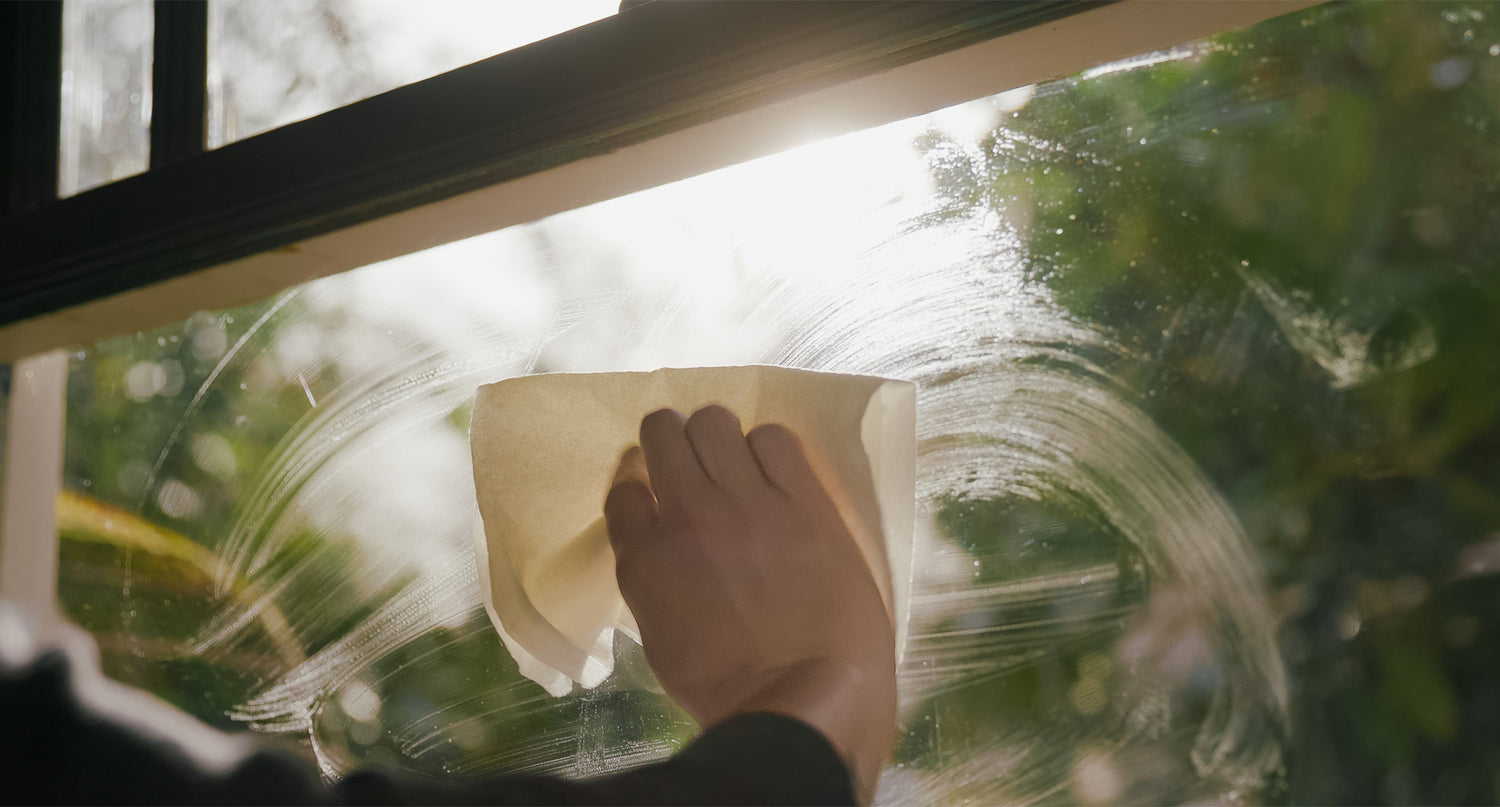 View of hand using paper towel to to clean window with soap.