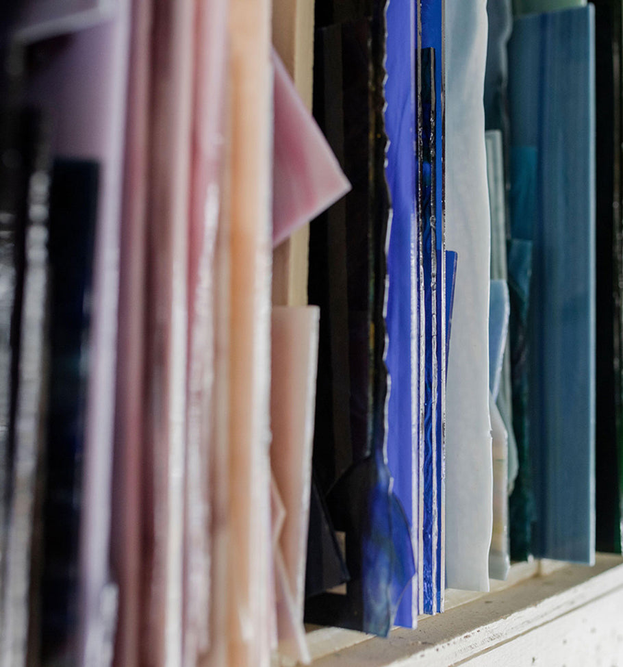 Shelf packed with glass stacked vertically in different colors.