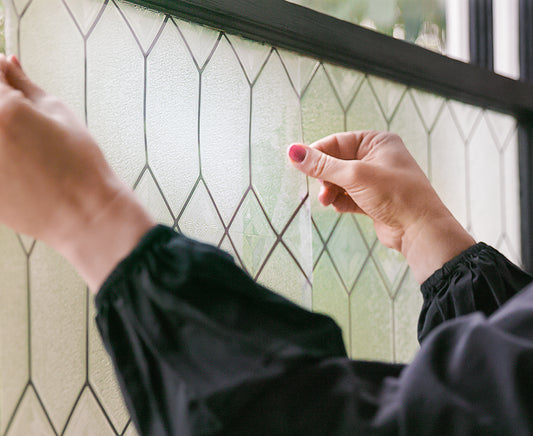 Woman's hands holding sheet of window film against window.