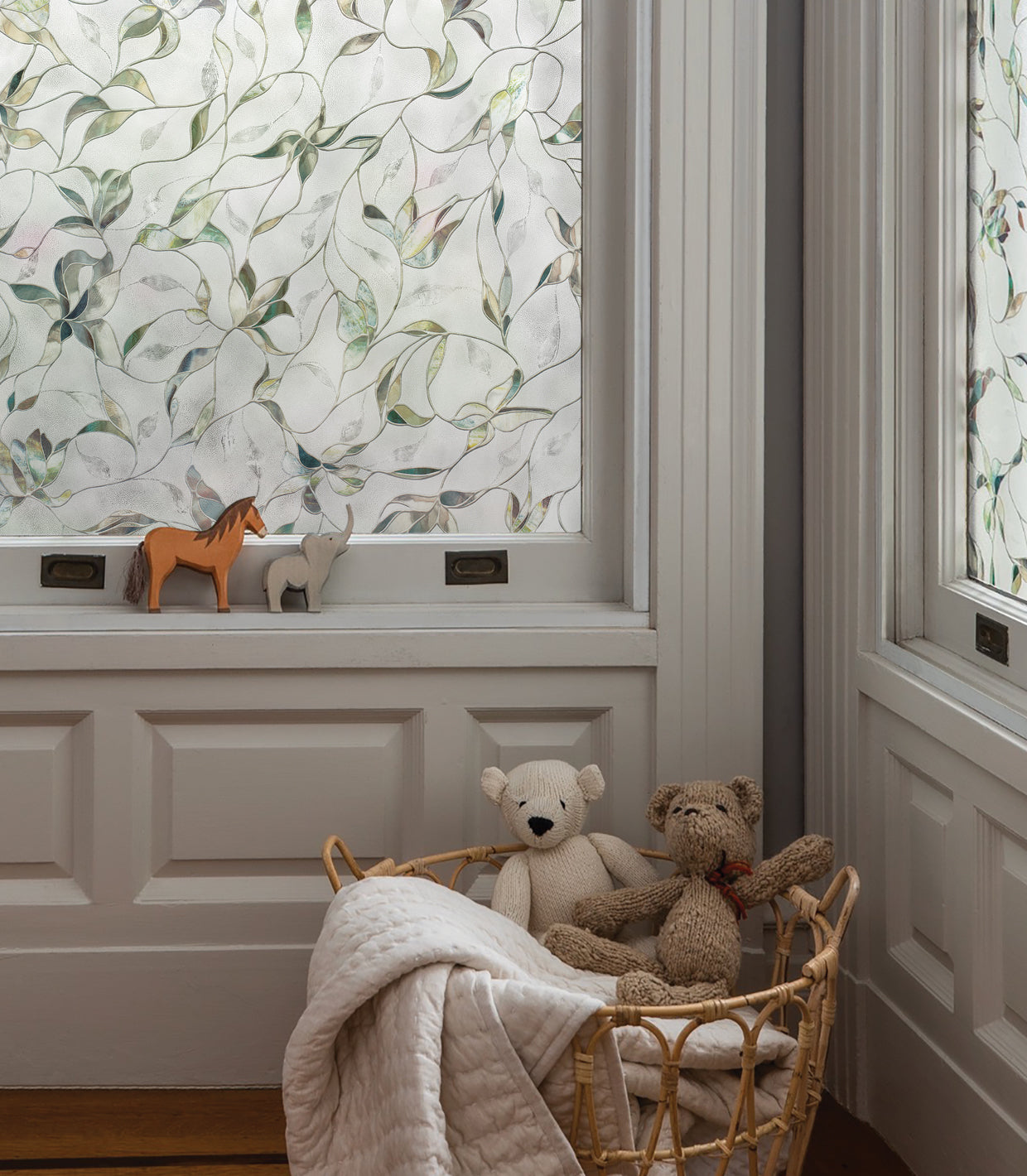 Child's room with light grey walls and a classic, upscale feel, featuring a wicker basket filled with stuffed animals and blankets, toy wooden horses on the sill, and both windows adorned with Artscape's Flight window film for a touch of elegance.