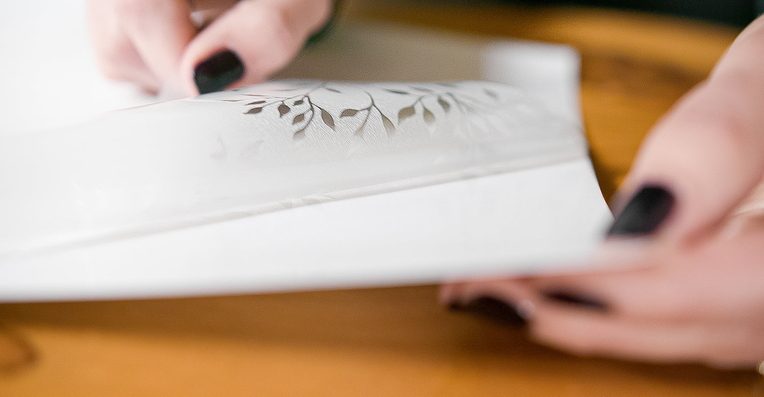 Hands removing paper backing from a sheet of white window film.